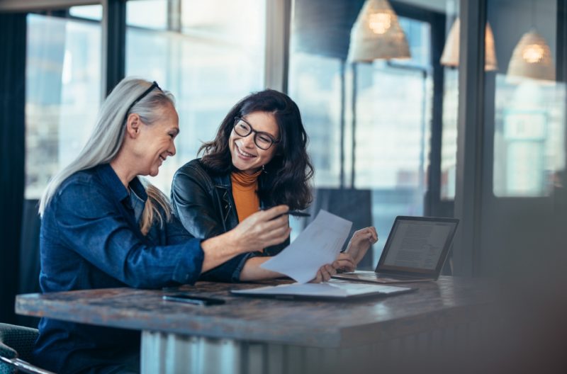 Two women working on a page together and smiling